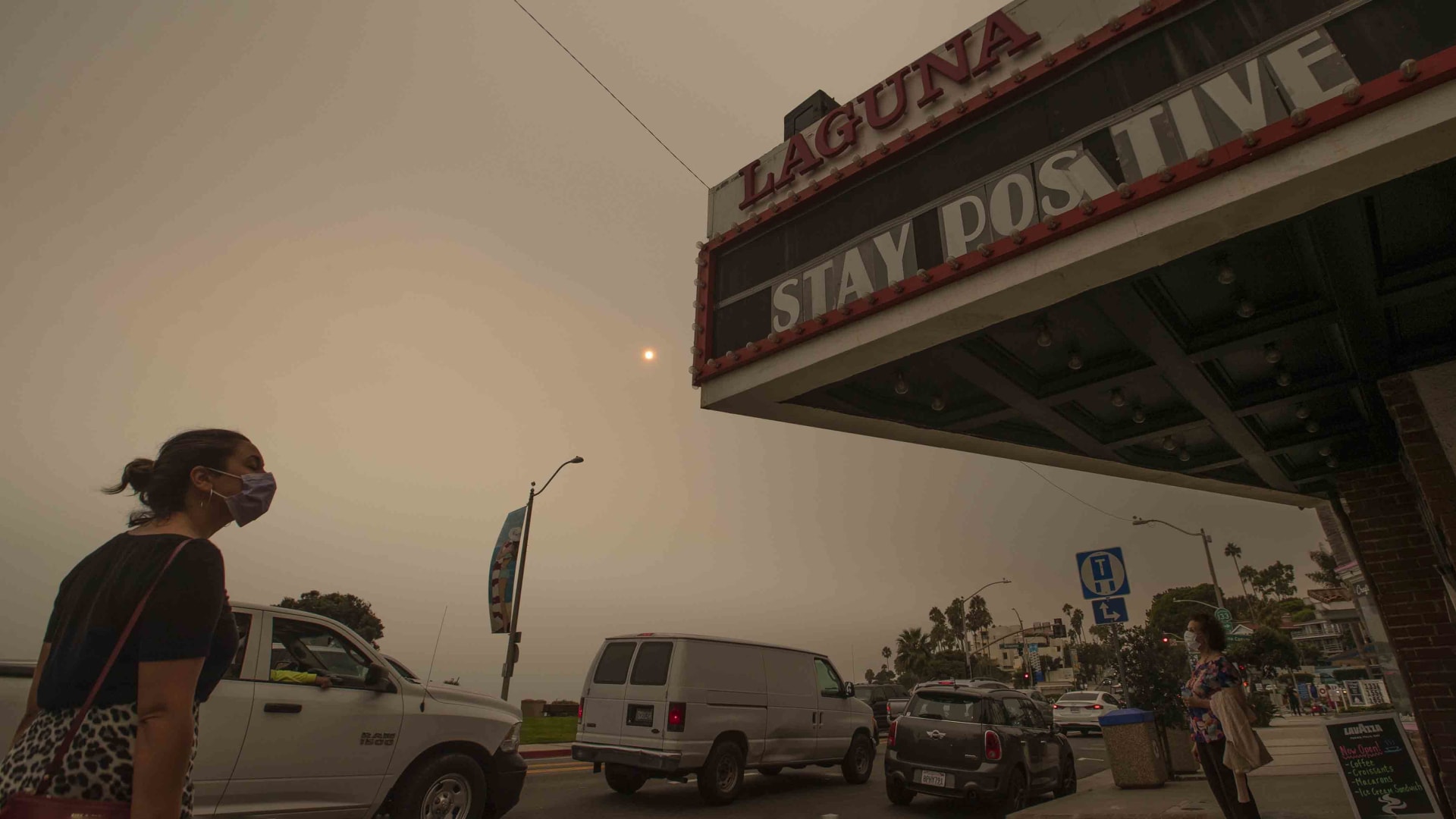 A woman walks past the The South Coast Cinemas building as the sun and sky are partially obscured with ash from Southland wildfires in Laguna Beach Thursday, Sept. 10, 2020.
